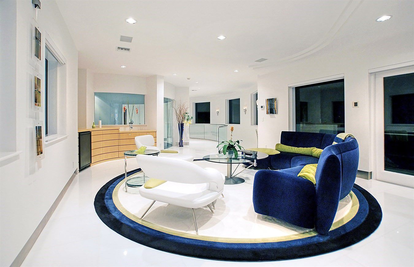 This living room was created using a combination of flat and semicircular architecture. They simply use a wooden cabinet to divide the space with other areas, even though it lacks a door, resulting in an open area. The color resemblance between the blue couch and the carpet, on the other hand, results in a unique space division, with the carpet covering the entire interior living room. In addition, the use of contemporary velvet and leather materials in this space creates a striking contrast.