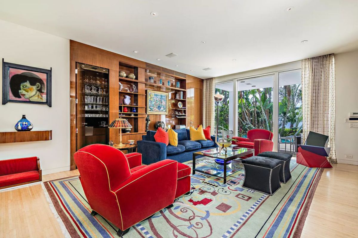 A space bursting with hues, forms, and patterns! There is a lot going on in a tiny space. The space is crowded by a vibrantly patterned rug, modern art, and a scattering of indoor plants. However, the more subdued hues like pure white walls, grey, and blue aid in reducing glare.