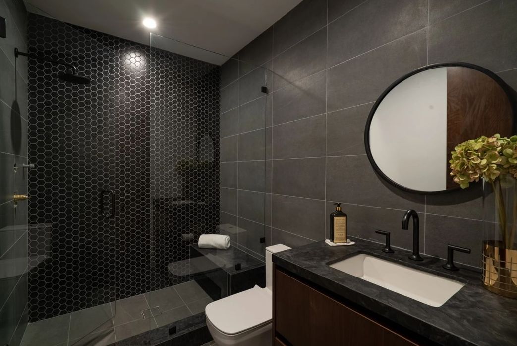 Contemporary bathrooms aren't usually white and sparkling. Dark may also be modern, as shown in this modern bathroom area dominated by a dark gray slate tile. The light wood furniture and white fixtures add much-needed light, color, and an organic sense. Take note of the minimal hardware and how the sink shapes mimic the size and form of the tiles.