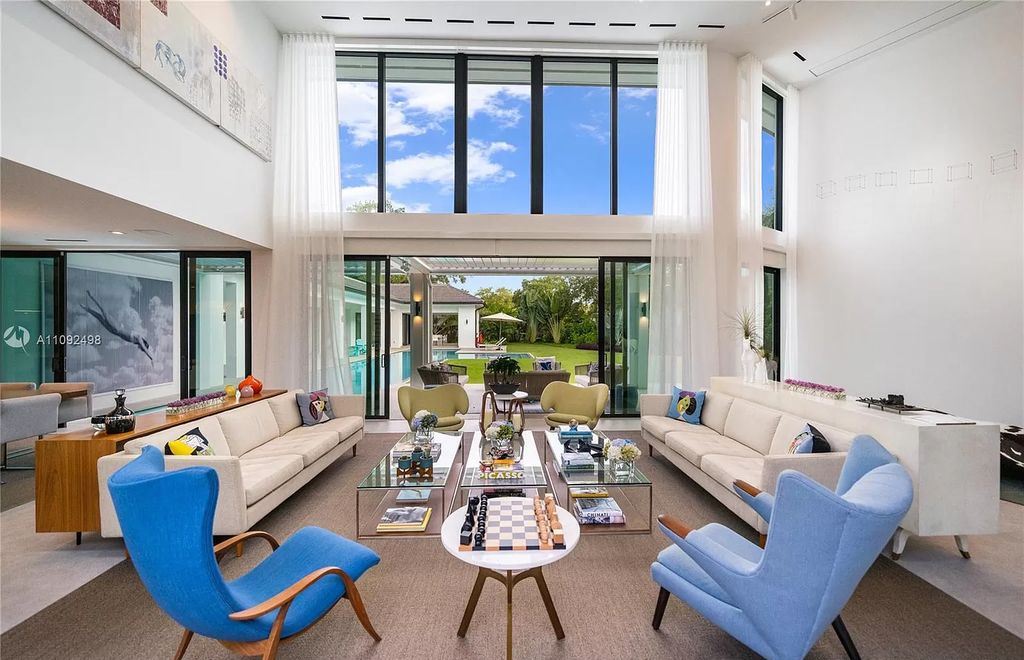 You can see the entire view of the double-height living room with fill-light coming in from this angle. They have arranged many interiors in this large room, including a long sofa set and two unique chairs. Create an attractive and eye-catching point in the creamy white space with two chairs in two different shades of blue. The seat cushion and blue chair shape have also been stylized to reflect a youthful and contemporary style.