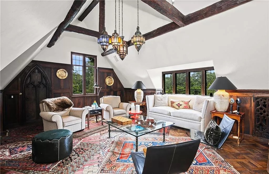 The variety of seats is the focal point of this eclectic living room ideas. Both the sofa, chair, and ottoman are made of the same high-quality black leather material. It's not unusual to see leather chairs on top of a brocade carpet because the owner's color palette is extremely subdued. The main door's style and the shape of the ceiling light give this space a wonderfully vintage feel.
