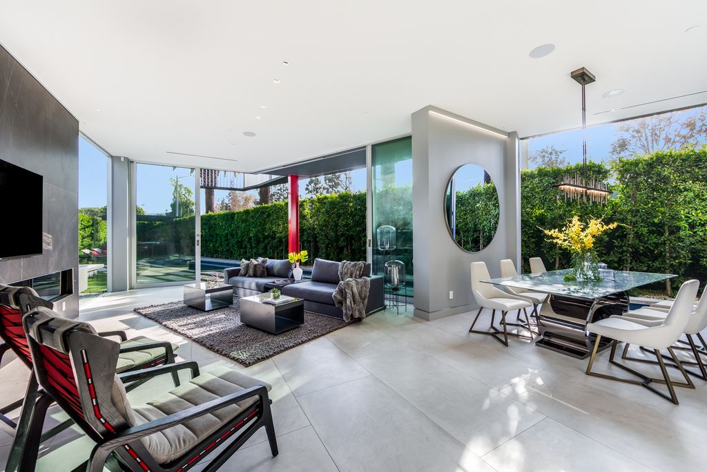 This living room is open in design and features a sizable glass door that quickly connects the indoor area to the patio outside. The light teak floorboards, accent wall made of grey marble, and white-painted ceiling and walls all make use of neutral lighting. The black couch, contemporary console, and various furniture accents prevent the room from being overly cluttered. This recreational area is made visually spacious and light by the outside view.