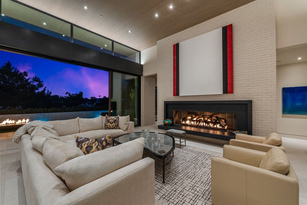 A wide open living area with a natural wood ceiling and glass walls creates a peaceful and modern atmosphere. The floor-to-ceiling windows provide enough of natural light while overlooking the spectacular outside vistas. The large gray sectional couch gives enough of seats for entertaining guests and relaxing in front of the fireplace. 