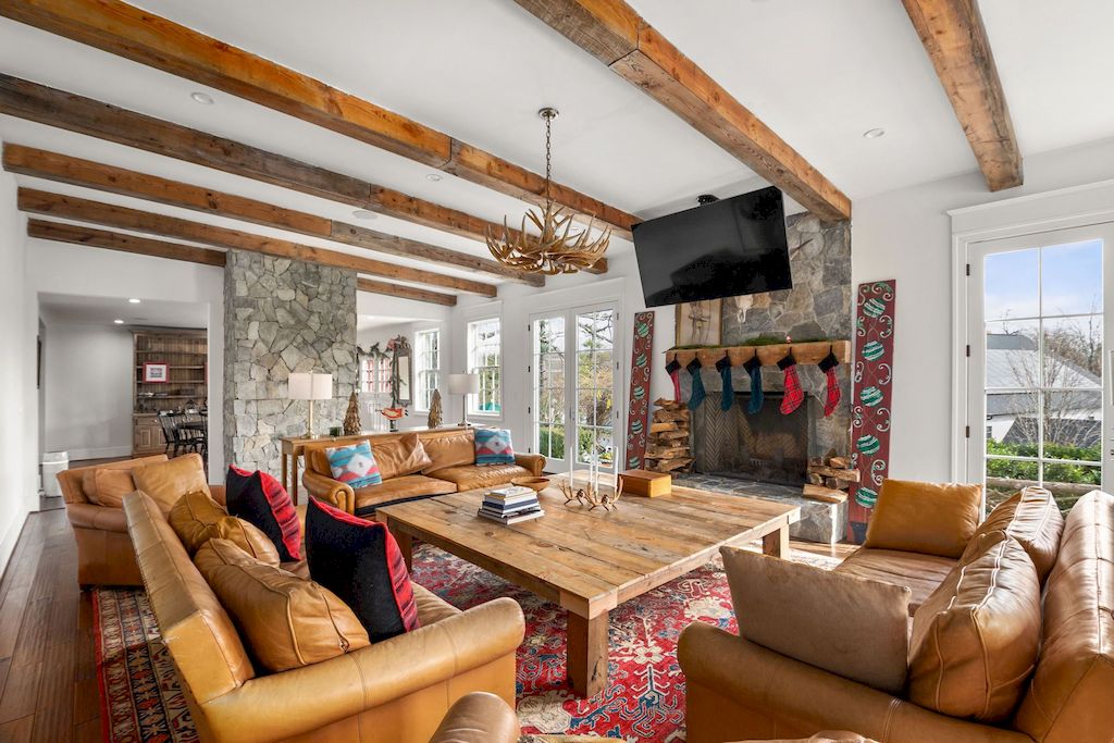 Warm colors, such as brown from the wood and red from the carpet, make up a cozy, cohesive living room. While some areas, such as the fireplace, are clad in cold large stones, the warm interior and wooden beam architecture have added gentle warmth from nature. It is impossible to overlook the appearance of a wooden center table, which, despite its simplicity, is an essential item if you are planning to build a country-style living room.
