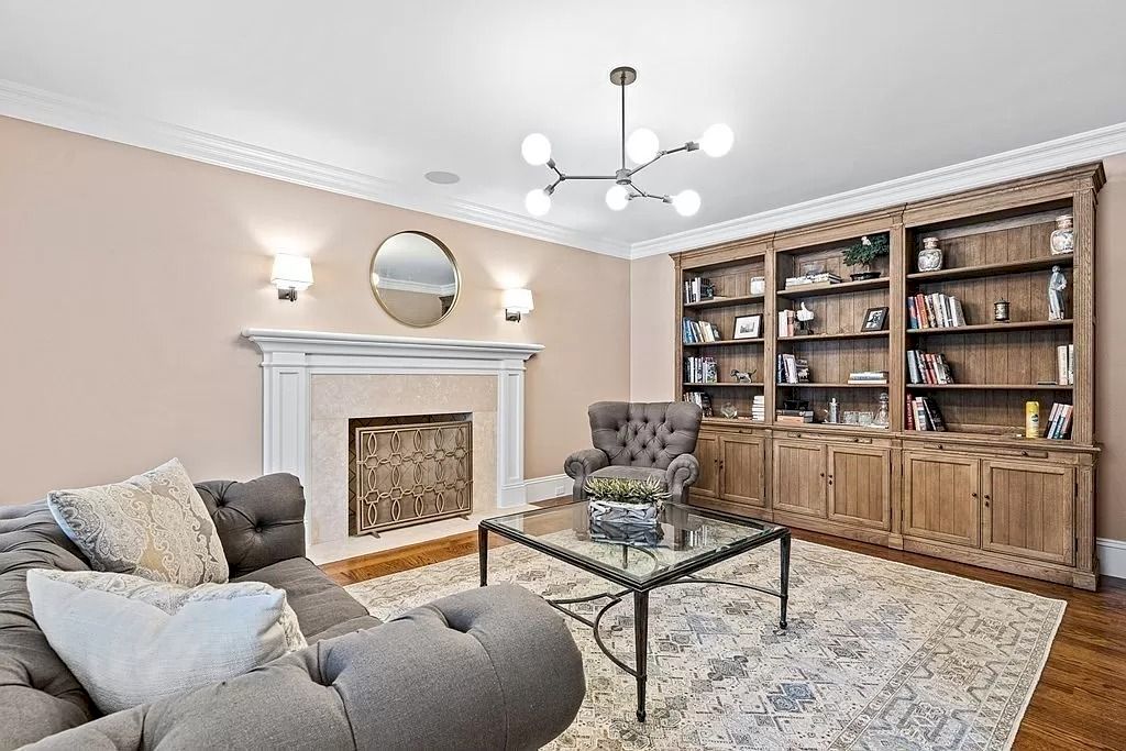 This living room's arrangement was created using a geometry exercise as a guide. The day table's strong glass lines and the circular mirror behind it contrast thanks to the precisely balanced shapes. The fireplace has a traditional focal point with a modern twist thanks to the herringbone pattern of white paint that is inserted into it.