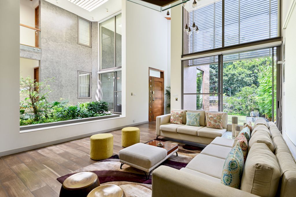 This elegant living room boasts high ceilings and expansive glass doors that let in plenty of natural light and offer a glimpse of the small garden outside. The rich leather sofas face the glass doors, inviting you to relax and enjoy the scenery. The decorative throw pillows add pops of color and texture to the otherwise neutral color scheme, while the patterned accent chairs provide a playful twist to the overall design.