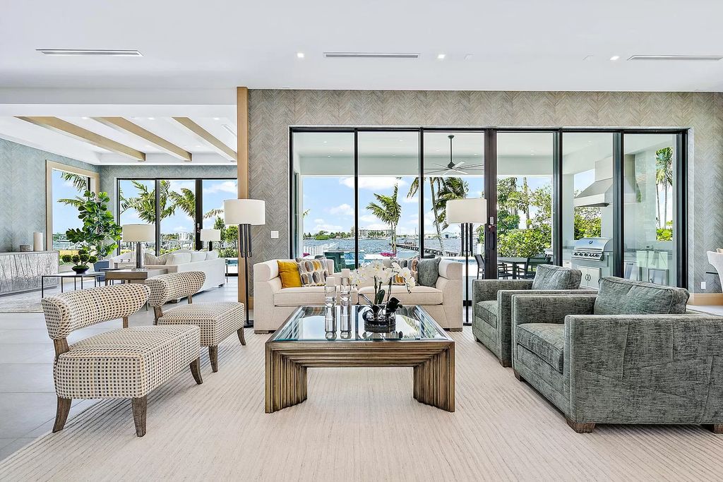 This artistically designed waterfront home in Lake Worth blends classic and modern elements seamlessly. The expansive glass doors on the front facade allow natural light to flood the space, creating an open and airy atmosphere. The custom sofas, upholstered in neutral linen, along with a unique coffee table, complement the overall paint style of the living room.