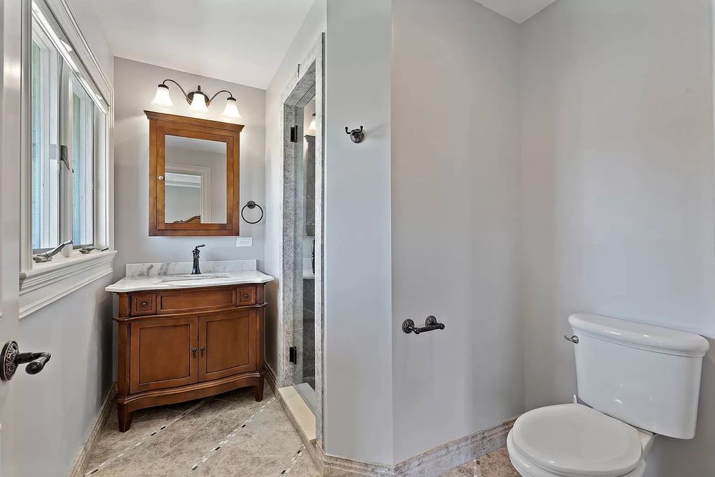 A rustic vanity, a barn door, and exposed ceiling beams are some examples of wooden features that provide warmth and texture to the space. Beige, gray, and white, as well as vintage-inspired fixtures like a cabinet, contribute to the rustic atmosphere.