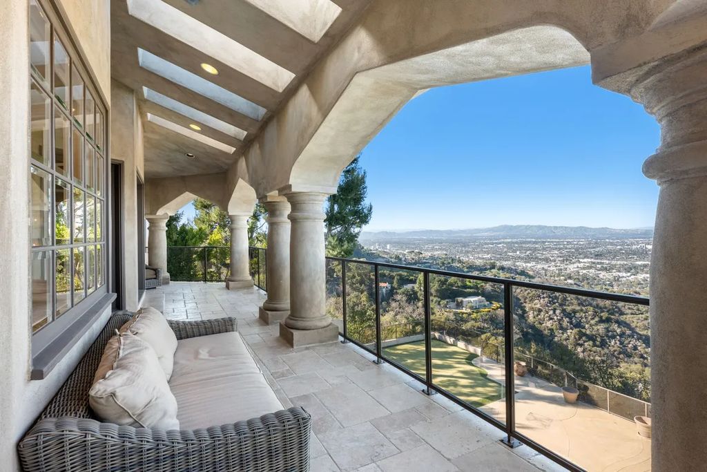 This exquisite estate offers breathtaking 360-degree views of the ocean sunsets, city lights, and Santa Monica mountains skyline, visible from its three stunning balconies. With over 9,300 square feet of space, this luxurious property boasts five bedrooms, seven bathrooms, three living rooms, formal and informal dining areas, and five beautiful fireplaces. The grand entrance through double doors leads to a dramatic 2-story foyer with 30-foot windows that flood the space with natural light, and limestone floors create an elegant touch.