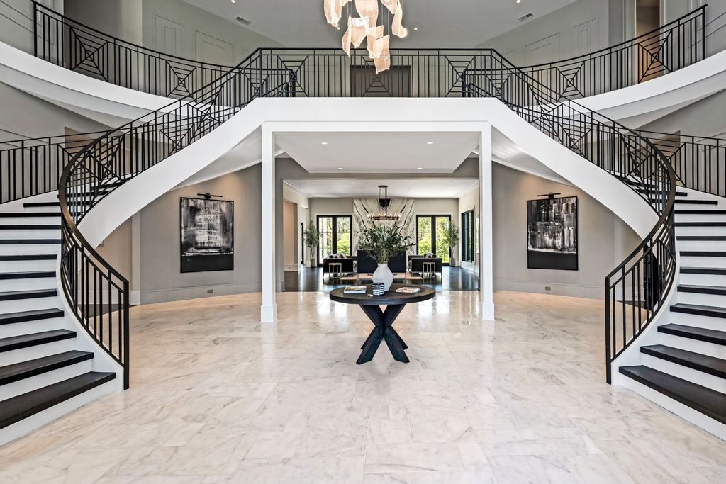 This luxurious home is located in a gated community and boasts 5 bedrooms, 9 bathrooms, and 19,561 square feet of living space on an 11-acre lot. The grand entrance leads to a spacious living room with stunning views of the green lawn outside.