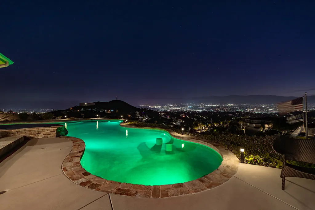 1045 Aquino Circle Home in Corona, California. Perched atop a private hill on over 4 acres, this 4,900 sqft custom home offers unparalleled views. Featuring 4 bedrooms, an office/bonus room, and a host of amenities, it was fully remodeled in 2016. Enjoy the remodeled interior, custom outdoor pool, spa, and entertainment area, RV hookup, detached 4-car garage with shop, A/C, and underground bunker.