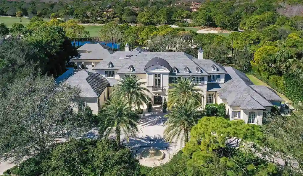 Aerial view of the exquisite French Country estate at 146 Bears Club Drive in Jupiter, FL, showcasing lush manicured grounds, a scenic residential lake, and panoramic golf course views.