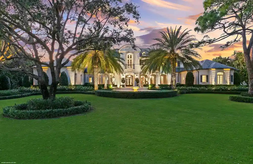 Aerial view of the exquisite French Country estate at 146 Bears Club Drive in Jupiter, FL, showcasing lush manicured grounds, a scenic residential lake, and panoramic golf course views.