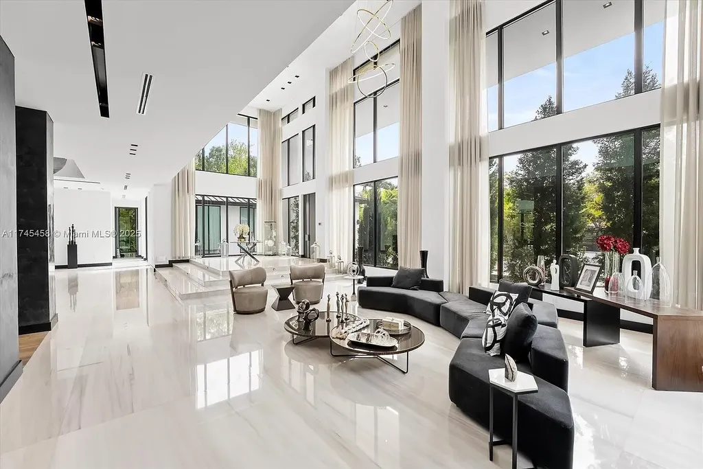 Spacious open-plan living room in 6555 SW 102nd St, featuring double-height ceilings, elegant marble floors, and floor-to-ceiling windows with natural light.