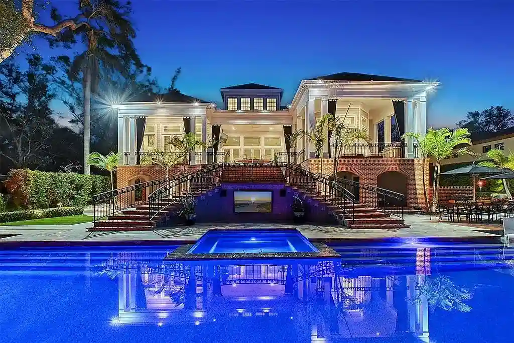 Elegant Georgian colonial waterfront estate at 1541 Bay Point Dr in Sarasota, FL featuring private dock, saltwater pool, theater room, and lush tropical landscaping.