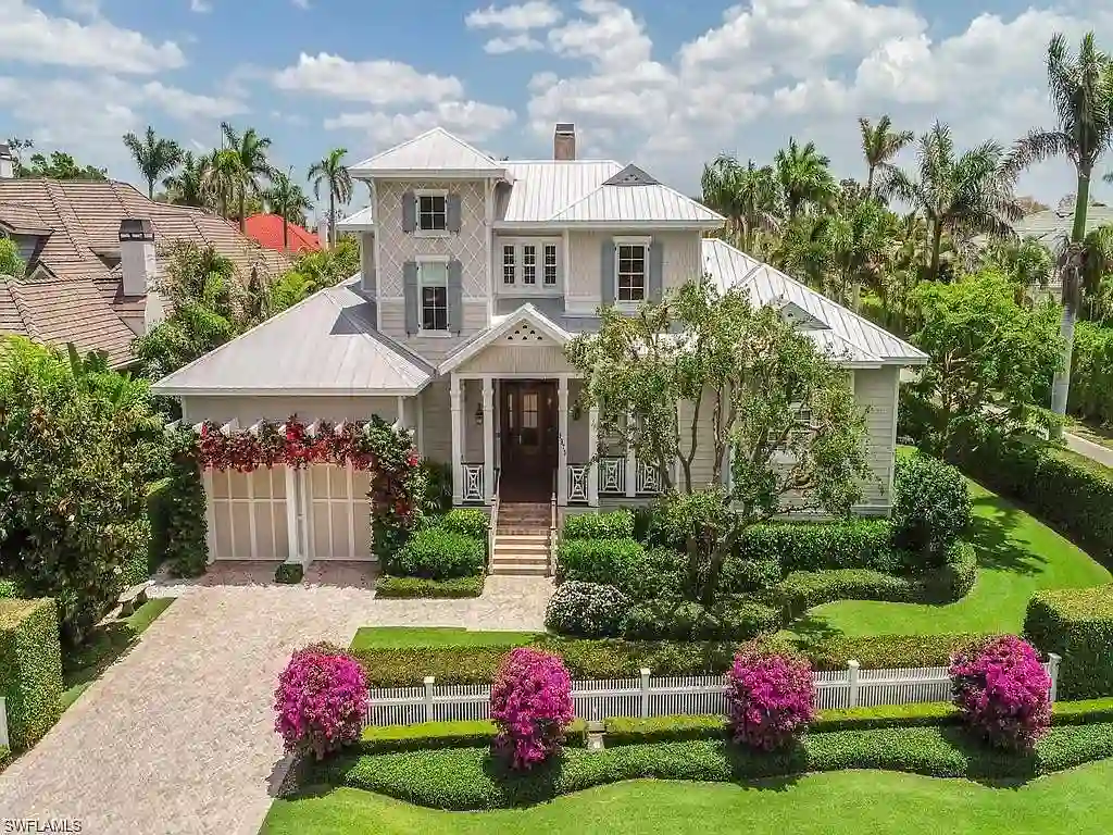 Front view of 1975 Gulf Shore Blvd S, Naples, FL: Old Florida coastal home with lush landscaping, guest house, and beach across the street.