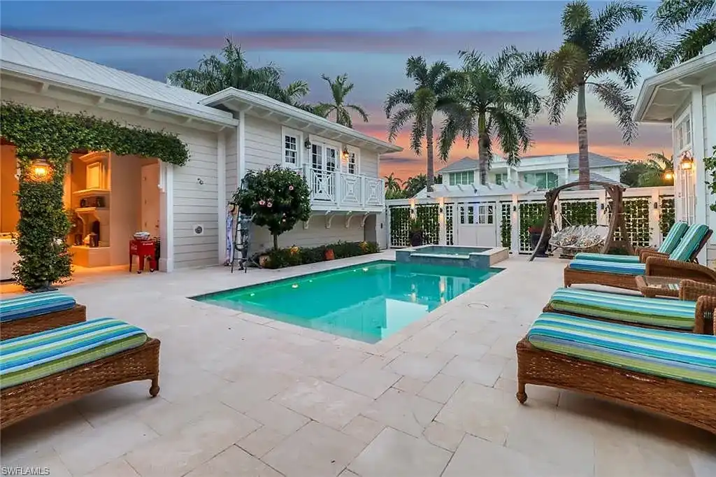 Front view of 1975 Gulf Shore Blvd S, Naples, FL: Old Florida coastal home with lush landscaping, guest house, and beach across the street.