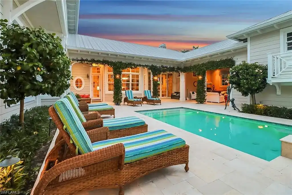 Front view of 1975 Gulf Shore Blvd S, Naples, FL: Old Florida coastal home with lush landscaping, guest house, and beach across the street.
